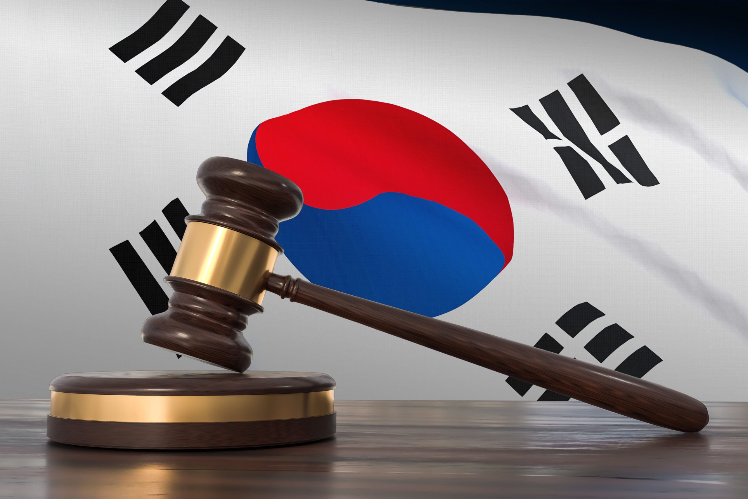 Wooden judge's gavel resting on a sound block in front of the South Korean flag, symbolizing law and justice.