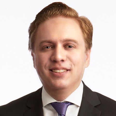 Professional headshot of Cody Wamsley smiling in a dark suit and patterned purple tie.