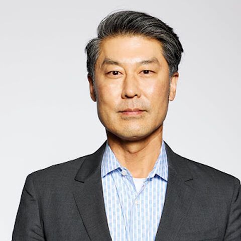 Professional headshot of Young-Sae Song wearing a dark blazer over a blue checkered shirt against a gray background.