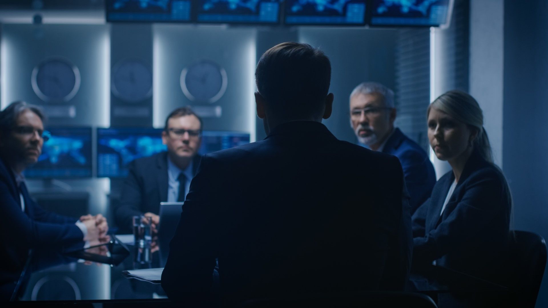 CISO addresses board members in a dark conference room with world maps and clocks displayed on screens behind them.