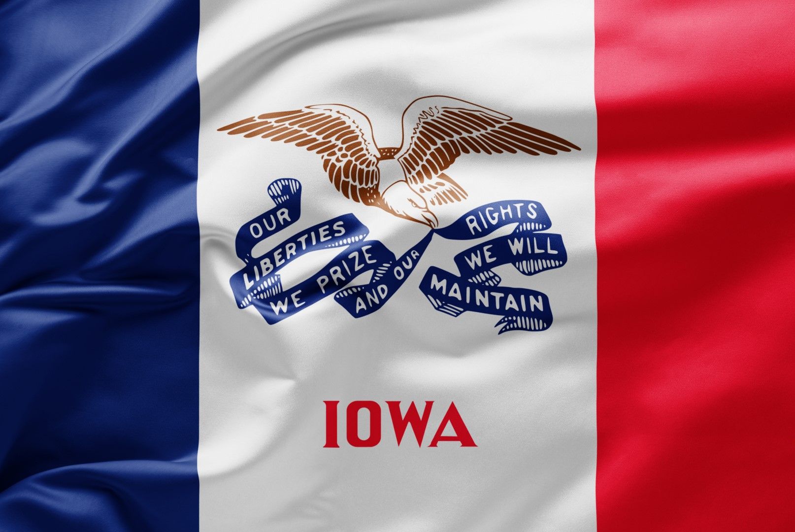 Waving Iowa state flag with blue, white, and red vertical stripes featuring a bald eagle holding a banner with the state
