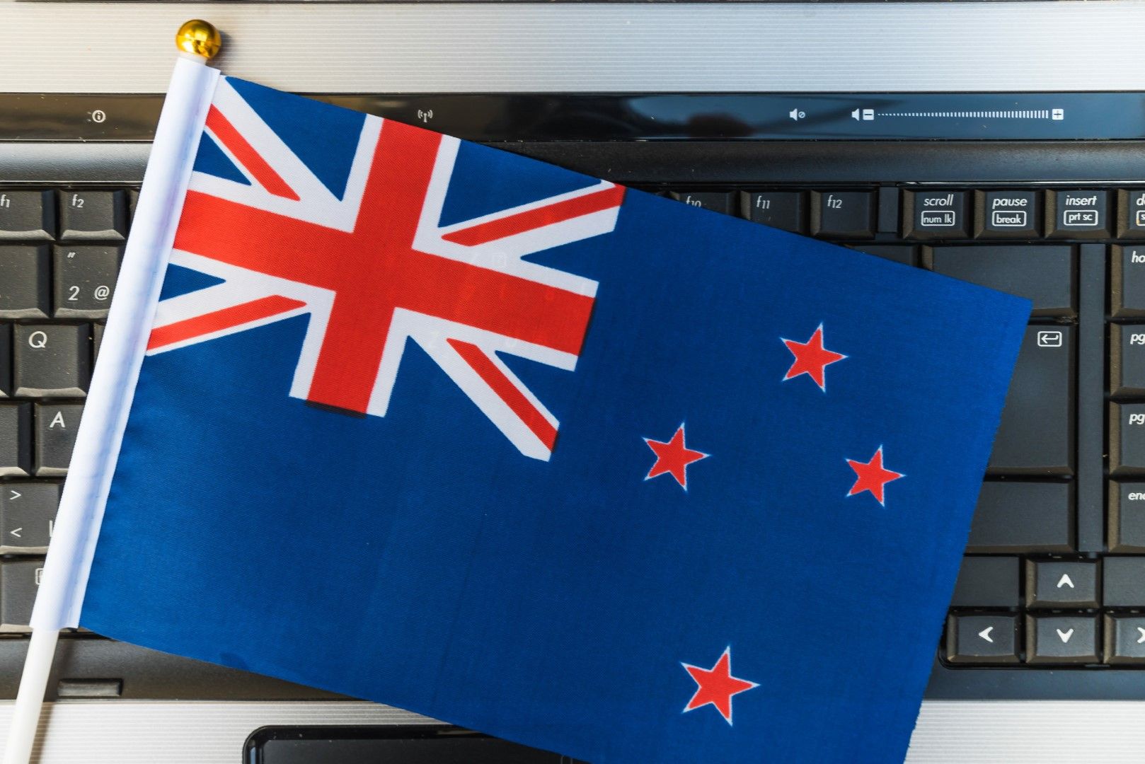 Small New Zealand flag on a stick resting across a black computer keyboard.