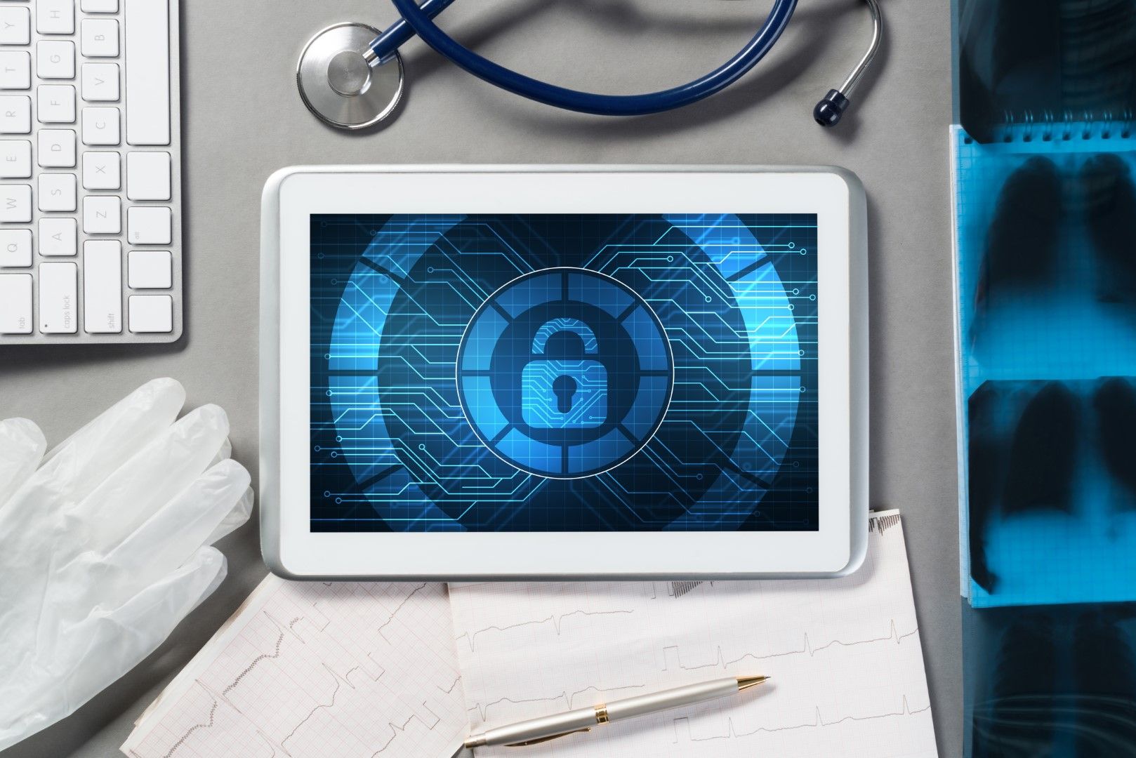 Tablet displaying a digital padlock icon surrounded by a stethoscope, keyboard, gloves, ECG readout, and chest X-rays.