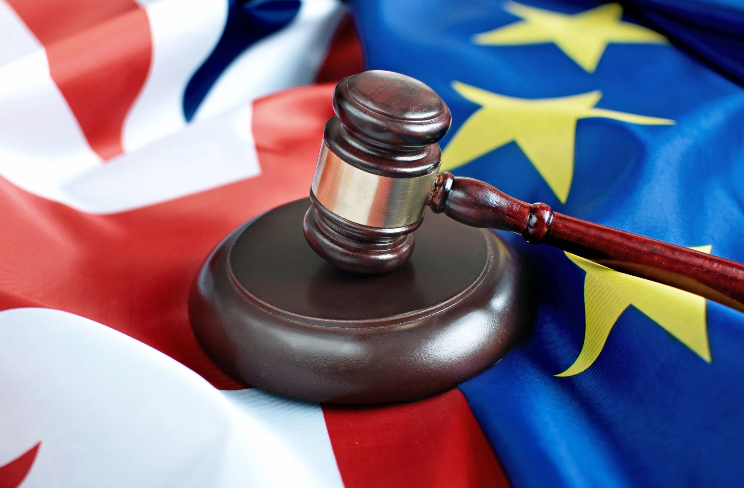 Wooden gavel resting on a sound block placed atop the UK Union Jack and European Union flags.