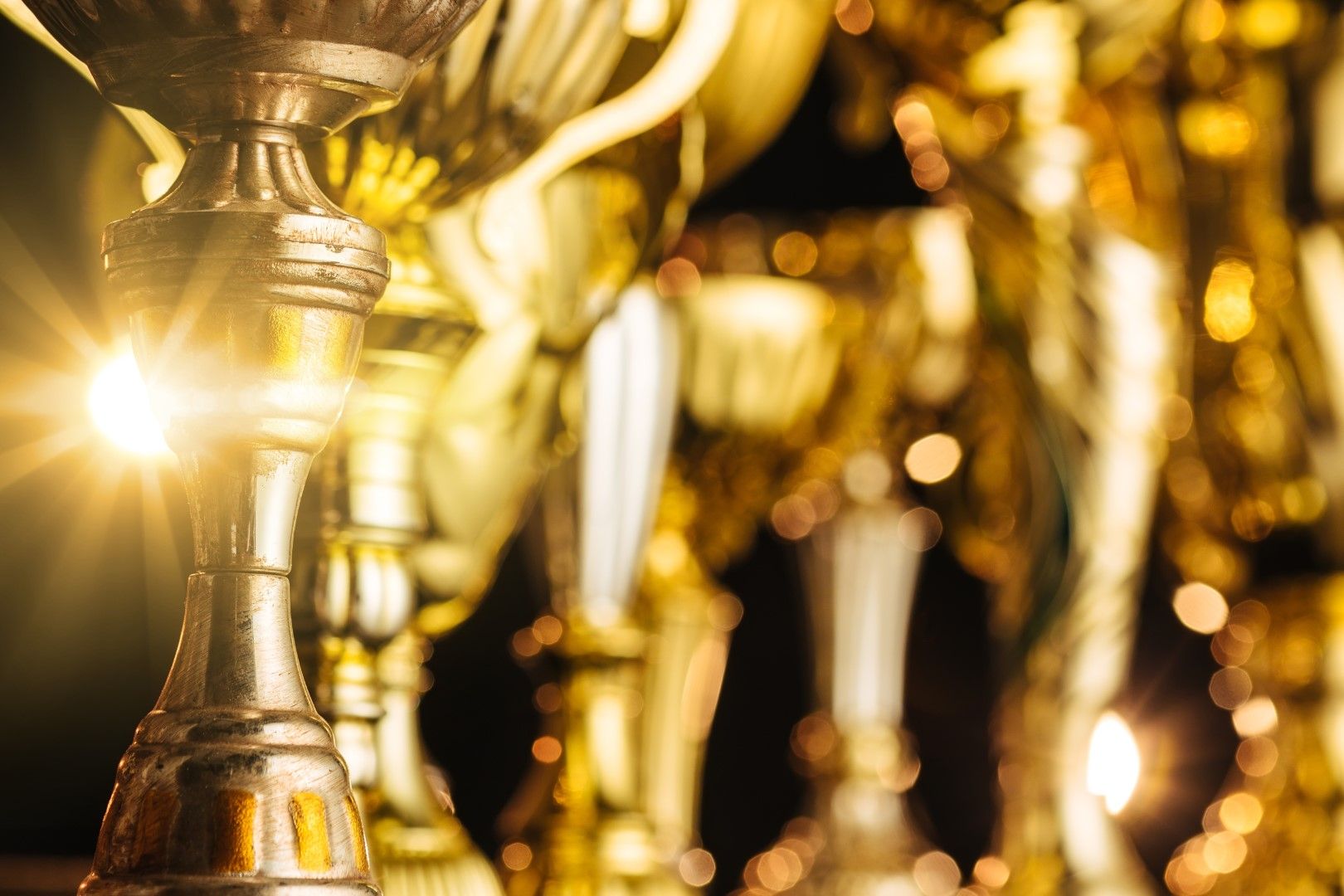 Gleaming golden trophies clustered together with sparkling light flares against a dark background.