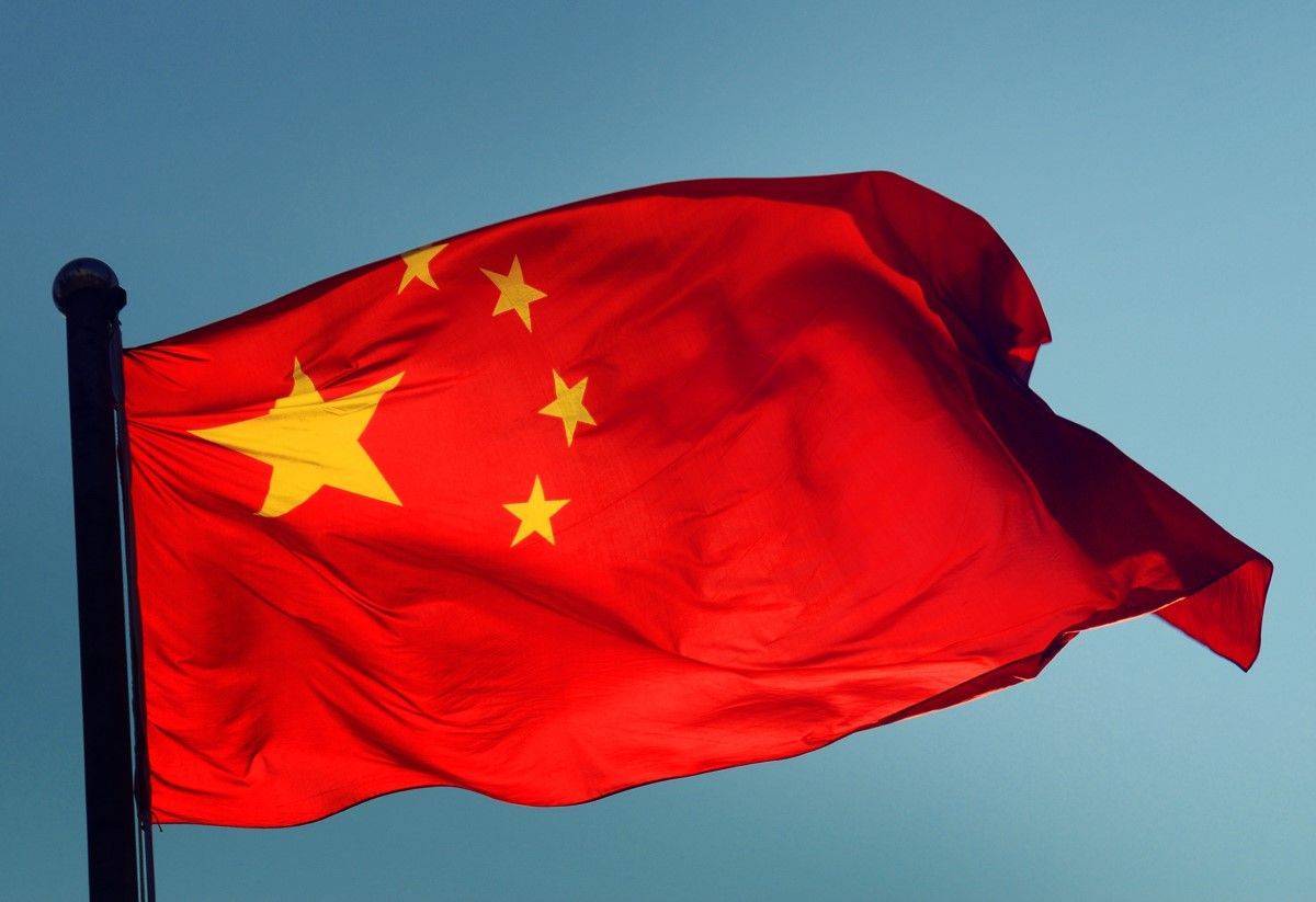 Red flag of China with five yellow stars waving against a clear blue sky.